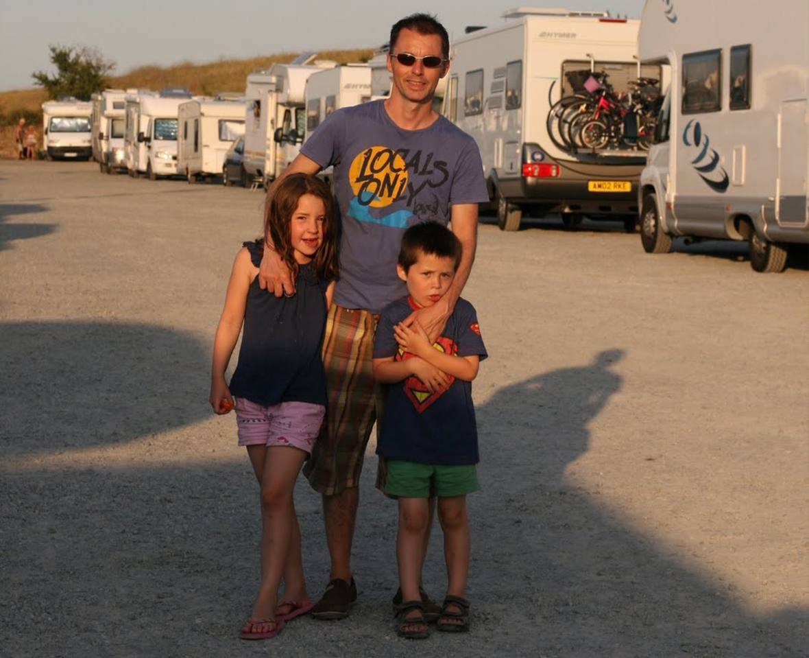 A man and two young children in a motorhome aire at sunset